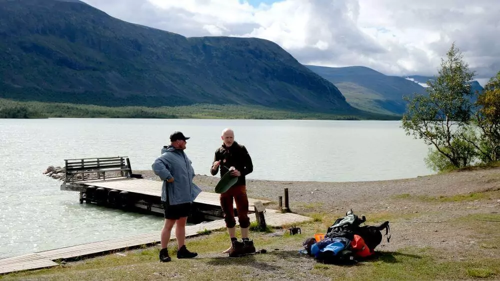 Paul talking to Magnus, a Fjällräven volunteer with a beautiful of the lake and mountains behind them